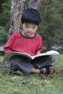 young boy reading outside